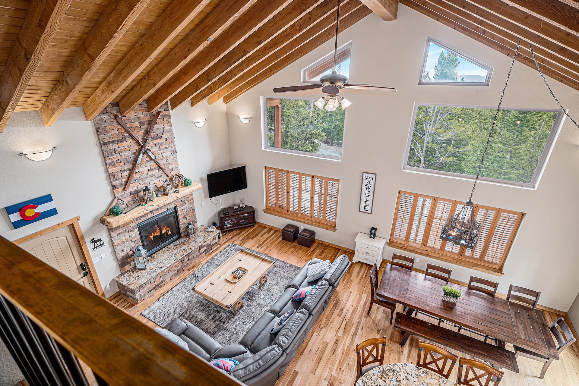 The great room seen from the loft: vaulted timber ceiling, stone fireplace with crossed skis and the dining table