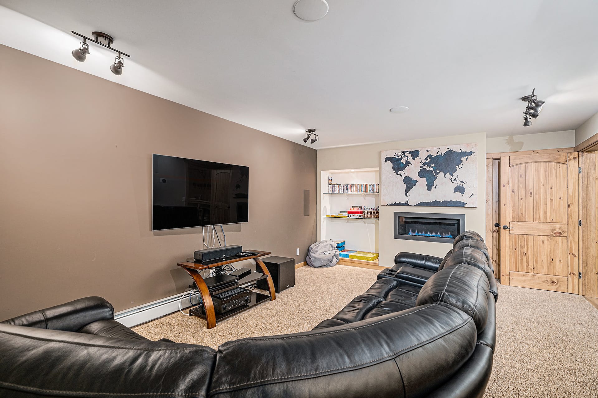 Home theater with a large wall TV, leather sectional and gas fireplace with a world map above